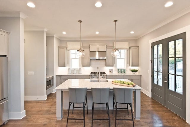 kitchen featuring crown molding, a center island with sink, under cabinet range hood, french doors, and a sink