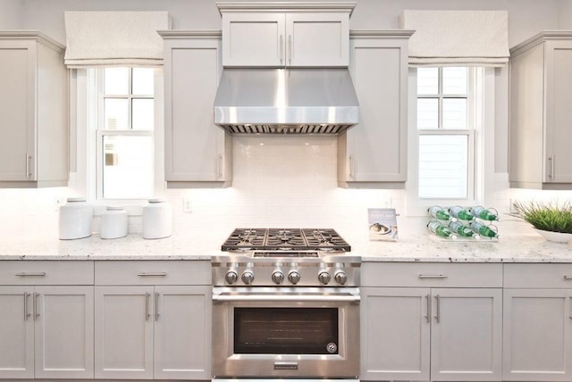 kitchen featuring decorative backsplash, high end range, gray cabinetry, light stone counters, and extractor fan