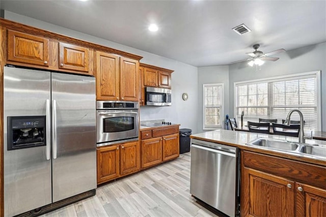 kitchen with appliances with stainless steel finishes, brown cabinetry, a sink, and visible vents