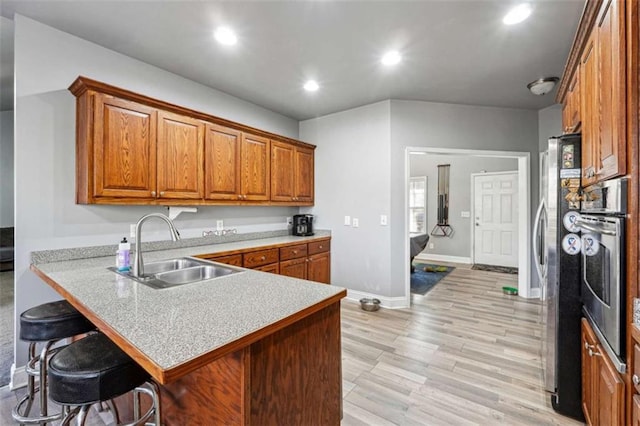 kitchen with brown cabinetry, a breakfast bar area, appliances with stainless steel finishes, a peninsula, and a sink