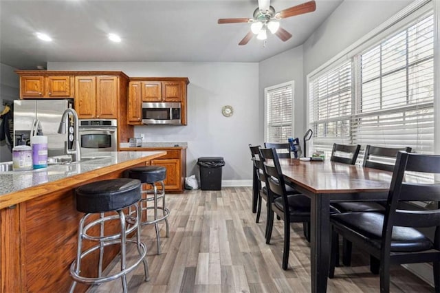 kitchen featuring baseboards, brown cabinetry, light wood-style flooring, a kitchen breakfast bar, and stainless steel appliances