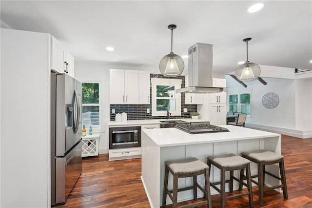 kitchen featuring a breakfast bar, island exhaust hood, dark wood finished floors, appliances with stainless steel finishes, and decorative backsplash