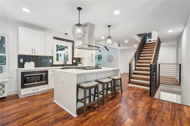 kitchen with tasteful backsplash, built in microwave, a kitchen bar, island range hood, and dark wood-style flooring