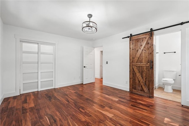 unfurnished bedroom featuring a barn door, baseboards, wood finished floors, and ensuite bathroom