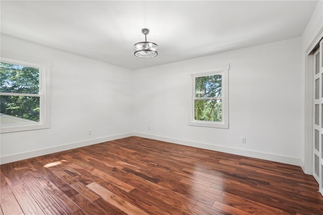 spare room featuring dark wood-type flooring, a notable chandelier, plenty of natural light, and baseboards