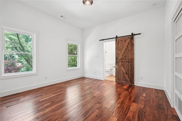 unfurnished bedroom featuring visible vents, baseboards, a barn door, and wood finished floors