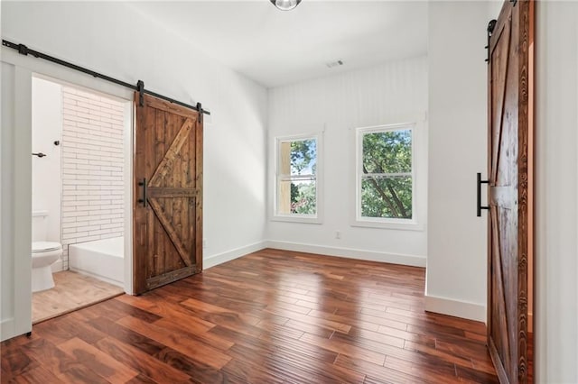 unfurnished bedroom featuring a barn door, wood finished floors, and baseboards