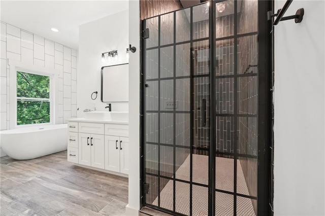 full bath with a soaking tub, recessed lighting, vanity, and wood finished floors