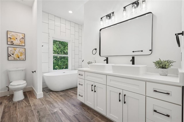 full bathroom with a sink, a soaking tub, wood finished floors, and double vanity