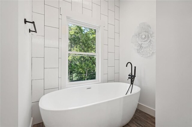 bathroom featuring a soaking tub, wood finished floors, and baseboards