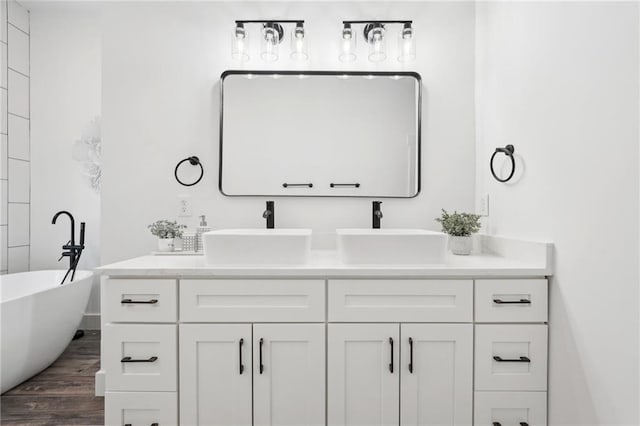 full bath with a sink, a soaking tub, wood finished floors, and double vanity