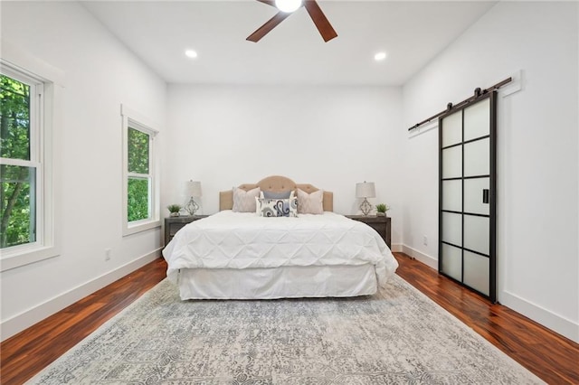 bedroom with a barn door, multiple windows, dark wood-style floors, and baseboards