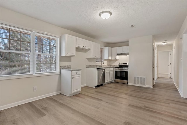 kitchen featuring appliances with stainless steel finishes, sink, white cabinets, light stone countertops, and light hardwood / wood-style floors