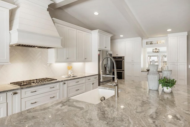 kitchen featuring custom range hood, a sink, light stone counters, white cabinetry, and stainless steel appliances