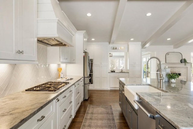 kitchen with a sink, beamed ceiling, white cabinets, and stainless steel appliances