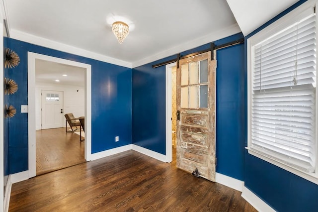 empty room with a barn door, baseboards, and wood finished floors