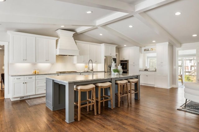 kitchen featuring premium range hood, a kitchen bar, lofted ceiling with beams, a sink, and stainless steel appliances