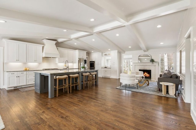 kitchen with vaulted ceiling with beams, open floor plan, appliances with stainless steel finishes, a kitchen breakfast bar, and custom exhaust hood