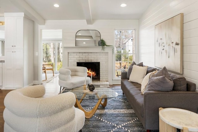 living area featuring wood finished floors, beamed ceiling, a fireplace, and a wealth of natural light