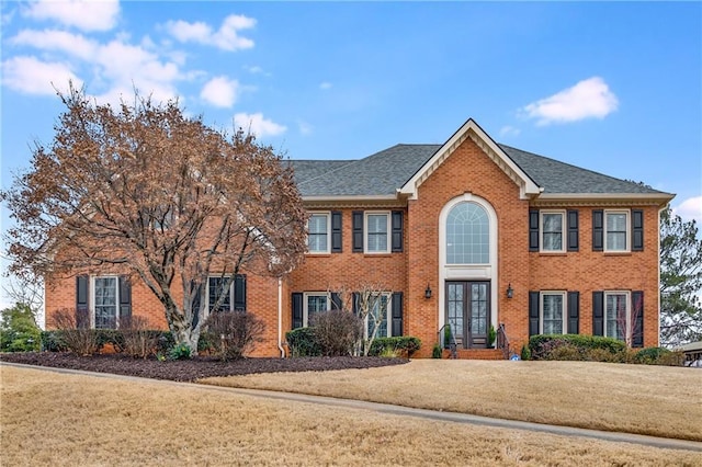 colonial home featuring brick siding, a front yard, and french doors