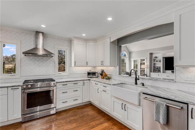 kitchen featuring dark wood finished floors, appliances with stainless steel finishes, ornamental molding, a sink, and wall chimney range hood