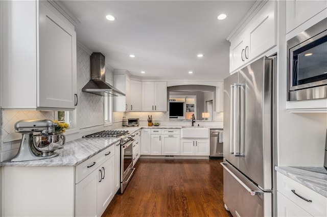 kitchen with high end appliances, white cabinets, a sink, and wall chimney exhaust hood