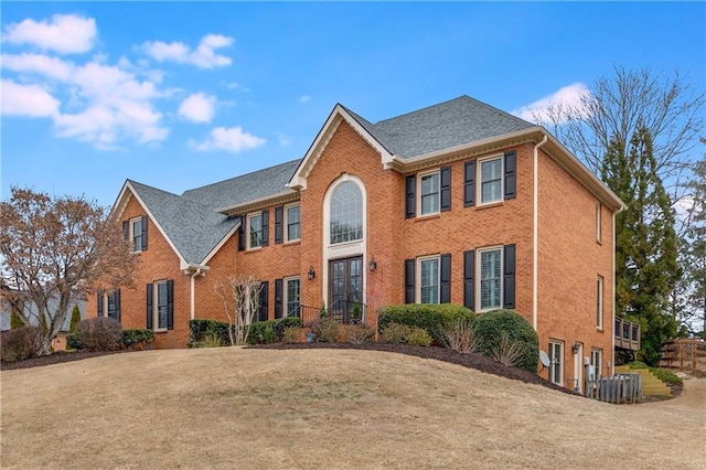 colonial home with brick siding, a front yard, and a shingled roof