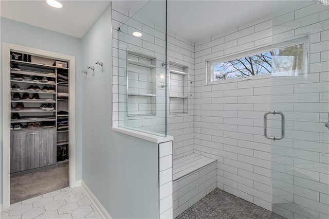 bathroom featuring a shower stall, baseboards, and a walk in closet