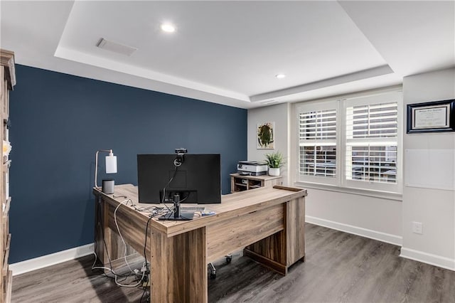 office with a tray ceiling, visible vents, baseboards, and wood finished floors