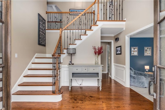 entryway featuring a high ceiling, wood finished floors, stairs, wainscoting, and crown molding