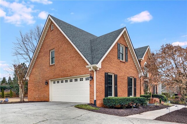 view of side of home with driveway, roof with shingles, an attached garage, and brick siding