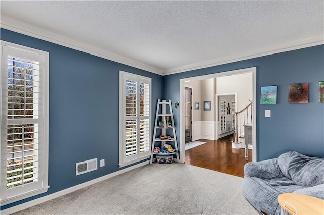 sitting room featuring a textured ceiling, visible vents, stairs, ornamental molding, and carpet