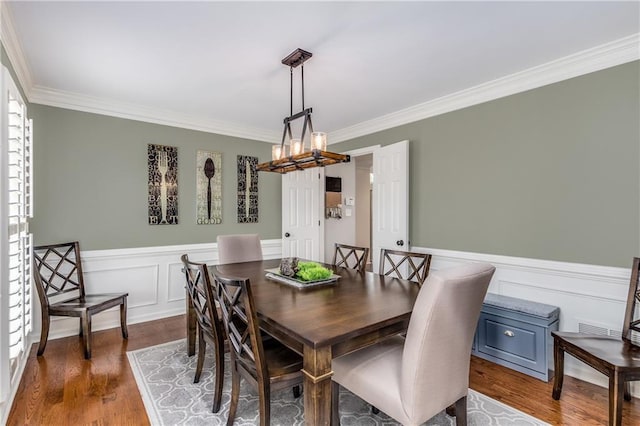 dining area with dark wood-type flooring, wainscoting, and crown molding