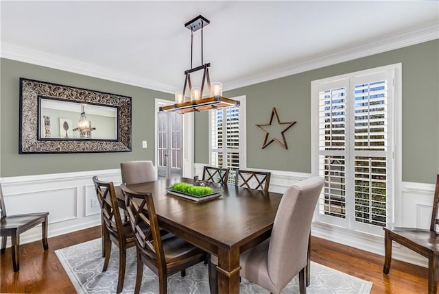 dining area with a decorative wall, a wainscoted wall, a notable chandelier, wood finished floors, and ornamental molding