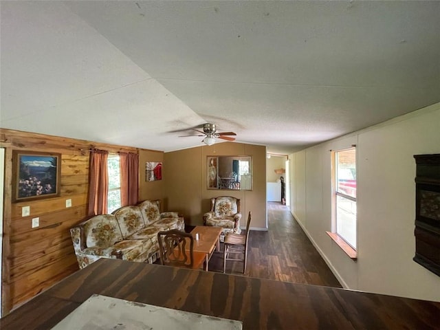 living area with ceiling fan, wood walls, vaulted ceiling, baseboards, and wood finished floors