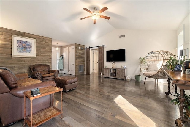 living room featuring dark wood-type flooring, ceiling fan, a barn door, and wooden walls