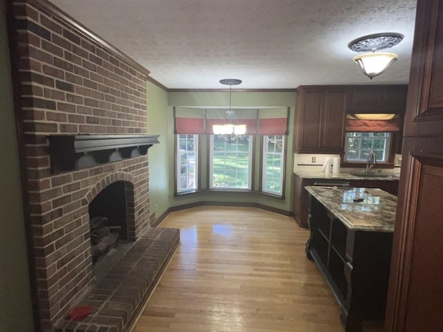 kitchen with a fireplace, a textured ceiling, ornamental molding, light hardwood / wood-style flooring, and a chandelier