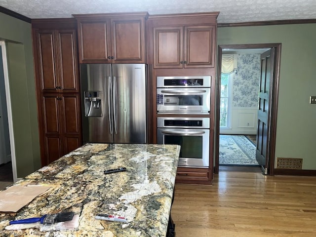 kitchen with hardwood / wood-style flooring, stainless steel appliances, ornamental molding, light stone counters, and a textured ceiling