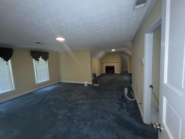 empty room with dark colored carpet, a textured ceiling, and vaulted ceiling