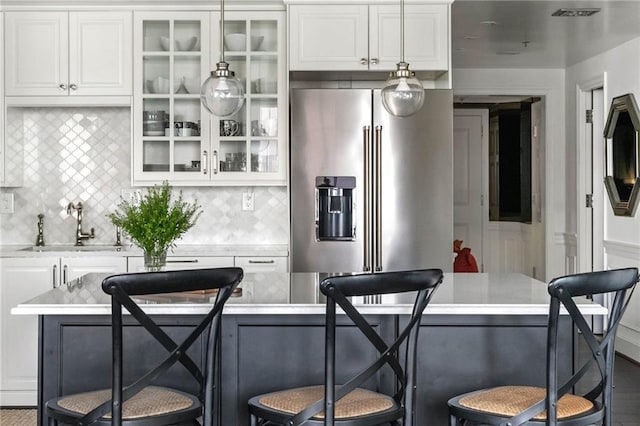 kitchen with decorative backsplash, high end refrigerator, white cabinets, and a kitchen bar