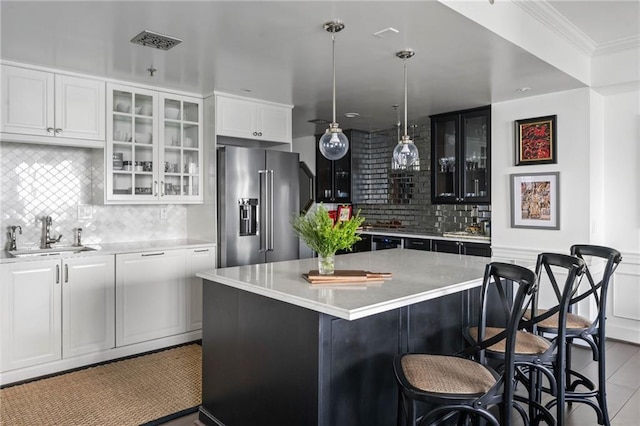 kitchen featuring a kitchen island, white cabinetry, sink, hanging light fixtures, and high end fridge