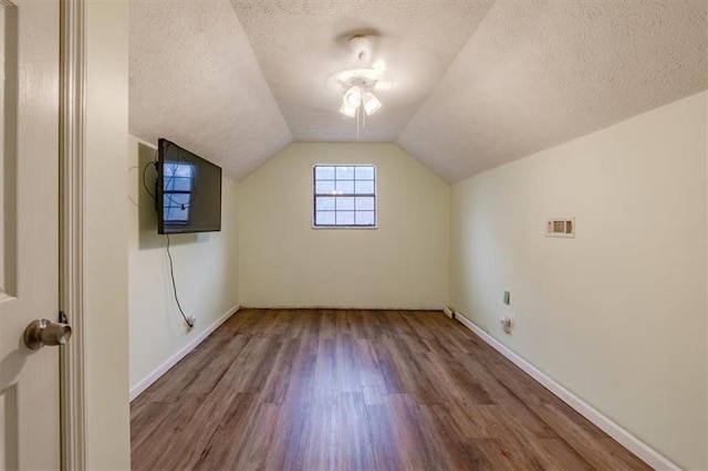 additional living space featuring vaulted ceiling, hardwood / wood-style floors, and a textured ceiling