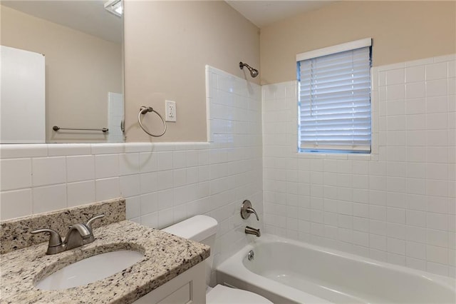 full bathroom featuring vanity, toilet, tiled shower / bath combo, and tile walls