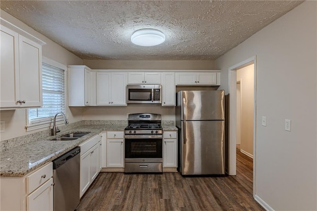 kitchen with dark wood-type flooring, sink, white cabinetry, appliances with stainless steel finishes, and light stone countertops