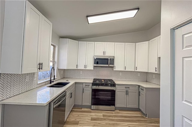 kitchen with lofted ceiling, gray cabinetry, a sink, appliances with stainless steel finishes, and tasteful backsplash