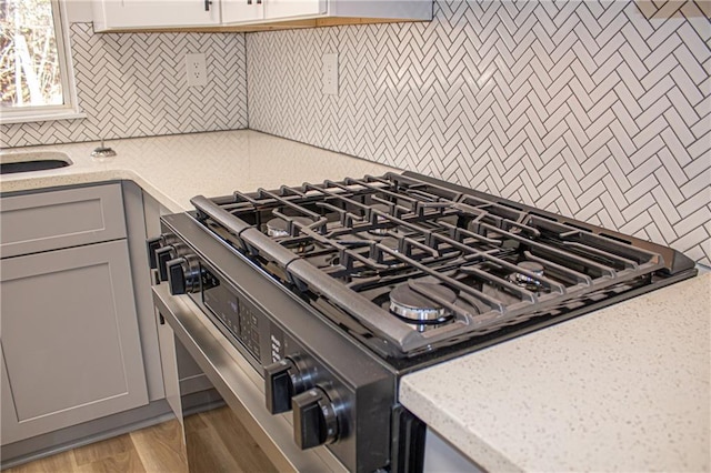 kitchen with gray cabinetry, light stone counters, backsplash, gas stove, and light wood-style floors