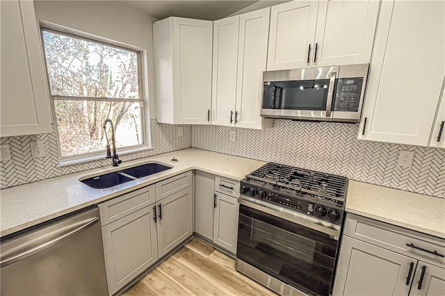 kitchen with light wood-style flooring, a sink, stainless steel appliances, decorative backsplash, and light stone countertops