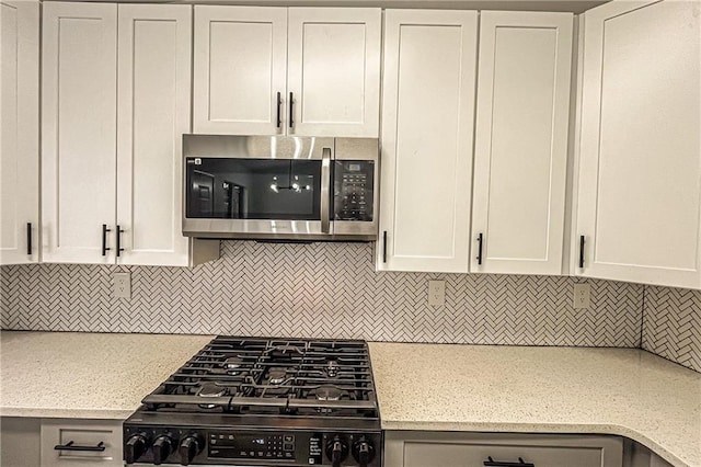 kitchen with stainless steel microwave, light stone counters, decorative backsplash, gas stove, and white cabinetry