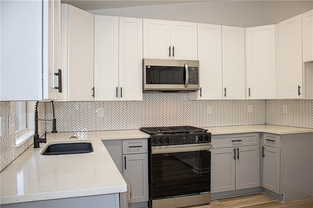 kitchen with stainless steel microwave, gray cabinetry, range with gas cooktop, light stone counters, and a sink