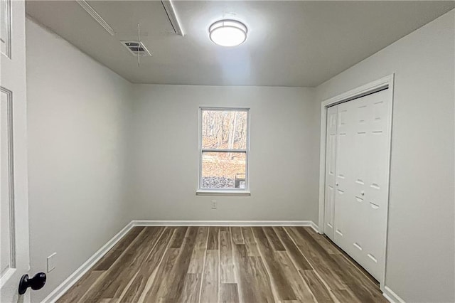 unfurnished bedroom with visible vents, baseboards, attic access, a closet, and dark wood-style floors